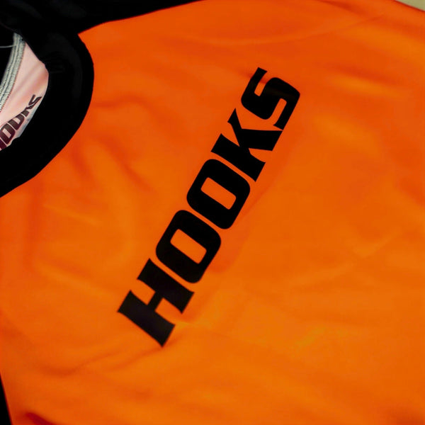 Hooks Kids 2026 Ranked BJJ Rash Guard Orange, close-up of chest showing large vertical black Hooks wordmark print