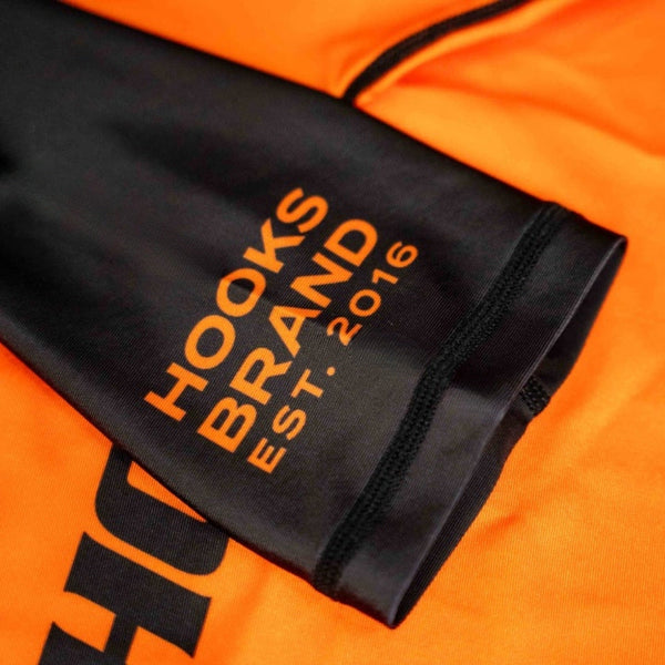 Hooks Kids 2026 Ranked BJJ Rash Guard Orange, close-up of black sleeve cuff with "Hooks Brand Est. 2016" orange print