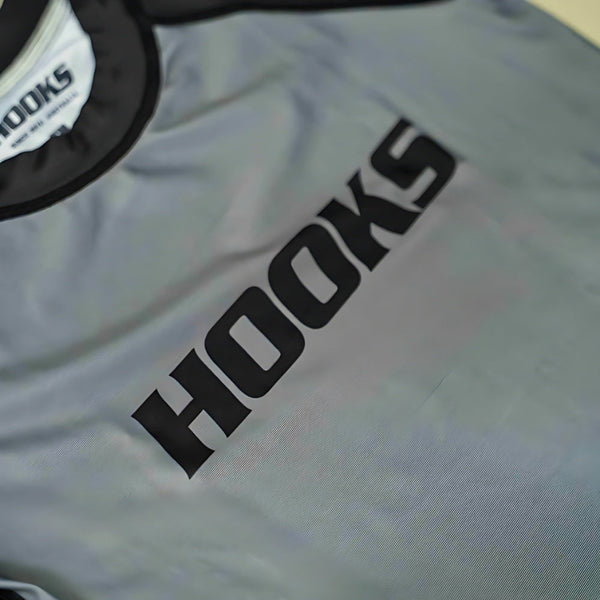 Hooks Kids 2026 Ranked BJJ Rash Guard Grey, close-up of chest showing bold black Hooks wordmark and black collar trim.