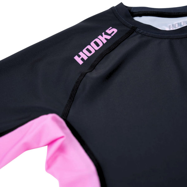 Hooks Short Sleeve Rash Guard Rose Noir, close-up of chest and sleeve showing pink panel, black stitching, and Hooks chest