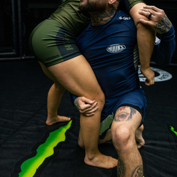 Hooks flex shorts worn during live grappling, shown alongside a navy Hooks rashguard in a BJJ training scenario