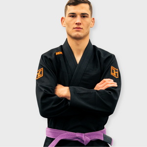 Person wearing a black martial arts uniform with logos on a light gray background