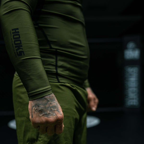 Hooks olive BJJ grappling shorts worn, close-up of sleeve logo detail and cuffed wrist on long-sleeve top