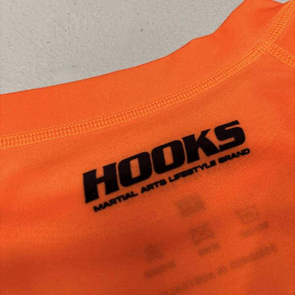 Hooks Kids Rash Guard Inferno, close-up of chest logo print and neckline stitching in orange fabric