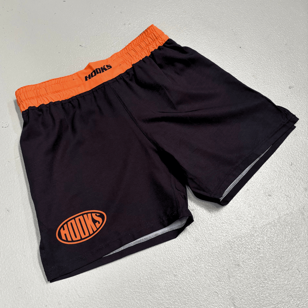 Hooks Sports Shorts Inferno, front flat lay showing black shorts with orange elasticated waistband and oval logo on left leg