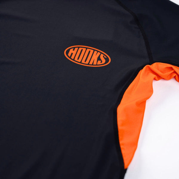 Hooks Short Sleeve Rash Guard Black Inferno, close-up of chest showing orange oval logo and orange side panel seam detail