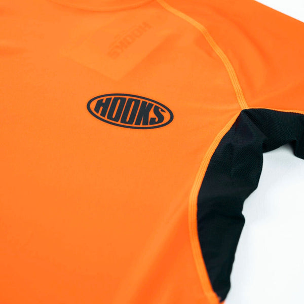 Hooks Inferno Short Sleeve Rash Guard, close-up of chest showing oval Hooks logo and black mesh side panel seam detail.