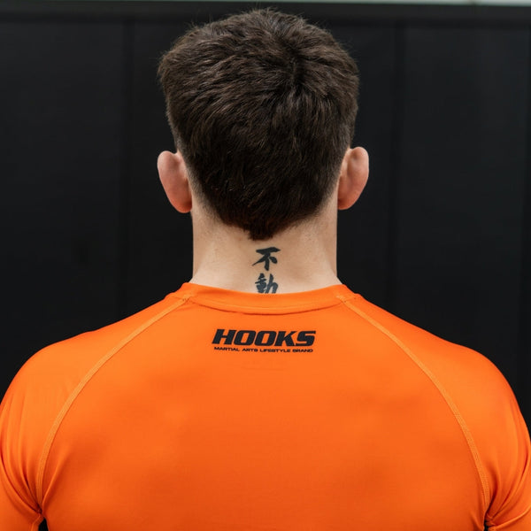 Hooks Inferno Short Sleeve Rash Guard, back view worn, showing black Hooks logo across upper back in orange