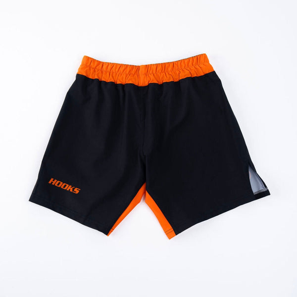 Hooks grappling shorts, front flat lay, black with orange waistband, hem accent, and logo; grey side panel visible