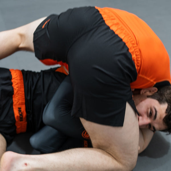Hooks Fusion Shorts Inferno, worn during ground grappling, showing black and orange colorblock panels in action