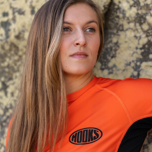 Hooks Inferno Short Sleeve Rash Guard, worn view showing orange body with black panel and chest logo