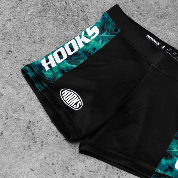 Hooks Women's Flex Shorts Jungle Reign, close-up of teal printed waistband and oval logo badge on black body