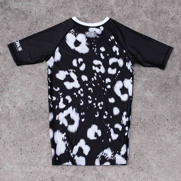 Hooks short sleeve rash guard, back flat lay with black and white leopard print body and solid black raglan sleeves