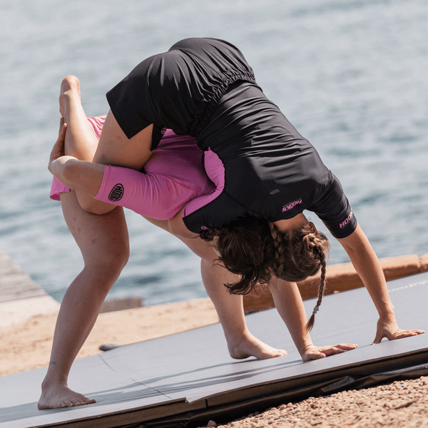 Hooks Rose Fusion Short Sleeve Rash Guard, worn by a child doing a backbend stretch outdoors alongside an adult