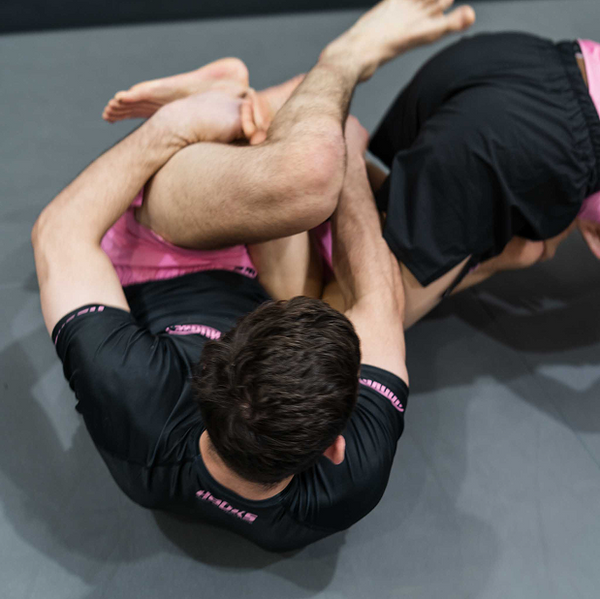 Hooks Short Sleeve Rash Guard Rose Noir, worn during live grappling, overhead view showing black body with pink branding