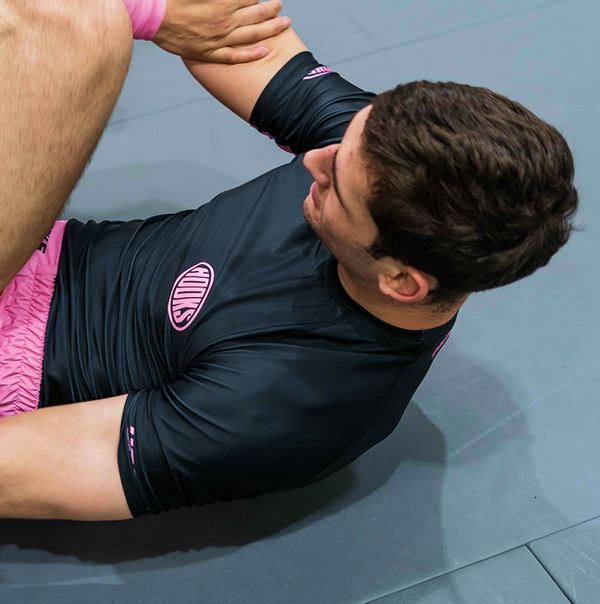 Hooks Short Sleeve Rash Guard Rose Noir, worn during grappling, showing chest logo patch and pink cuff detail from above