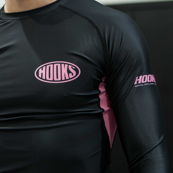 Hooks Long Sleeve Rash Guard Rose Noir, close-up of chest logo and sleeve branding, worn, showing pink side panel detail