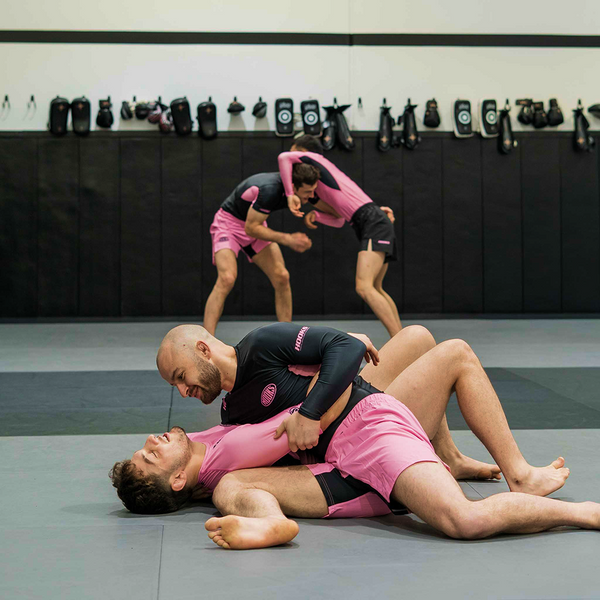 Hooks Rose Fusion Shorts worn during live grappling on gym mats, with two more athletes training in the background.