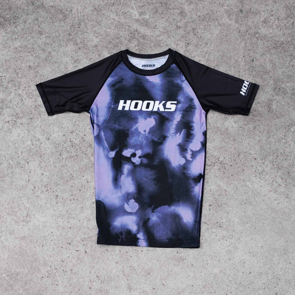 Hooks short sleeve rash guard, front flat lay, violet haze tie-dye body with black raglan sleeves and white Hooks chest logo