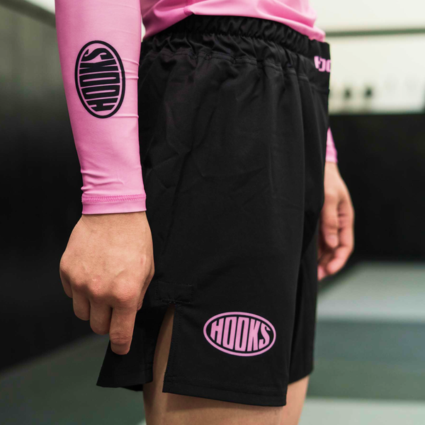 Hooks Fusion Shorts Rose Noir, side view worn, black shorts with pink oval logo on hem, paired with matching pink Hooks rash