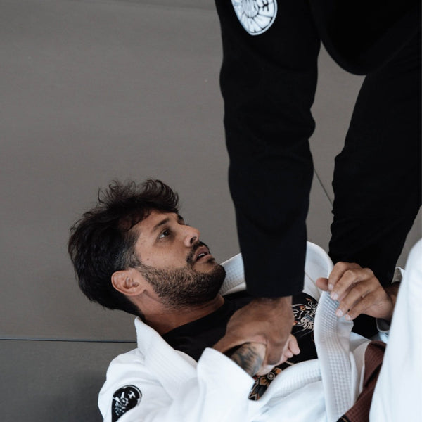 Martial arts training session with a person in a white gi and brown belt on the ground, gripping the sleeve of an opponent in a black gi