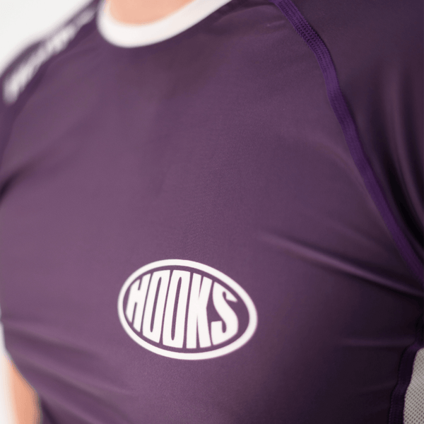 Hooks Fusion Short Sleeve Rash Guard in Plum, close-up of chest logo and raglan seam detail, worn.