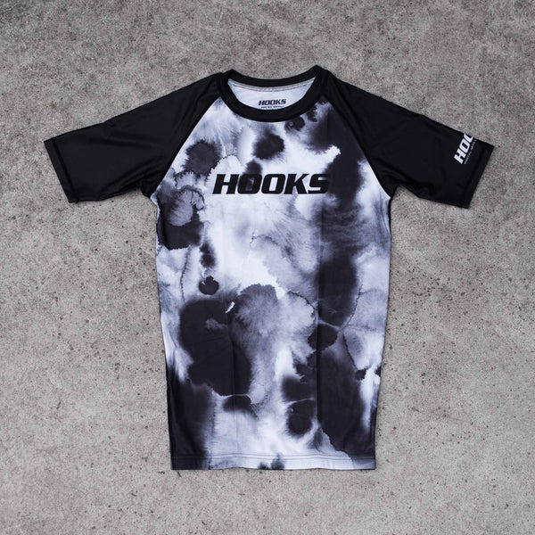 Hooks short sleeve rash guard, front flat lay, black and white watercolour mist print body with solid black raglan sleeves